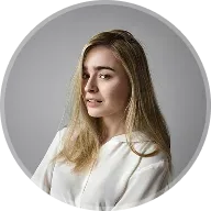 Young woman with long blonde hair wearing a white blouse against a gray background.
